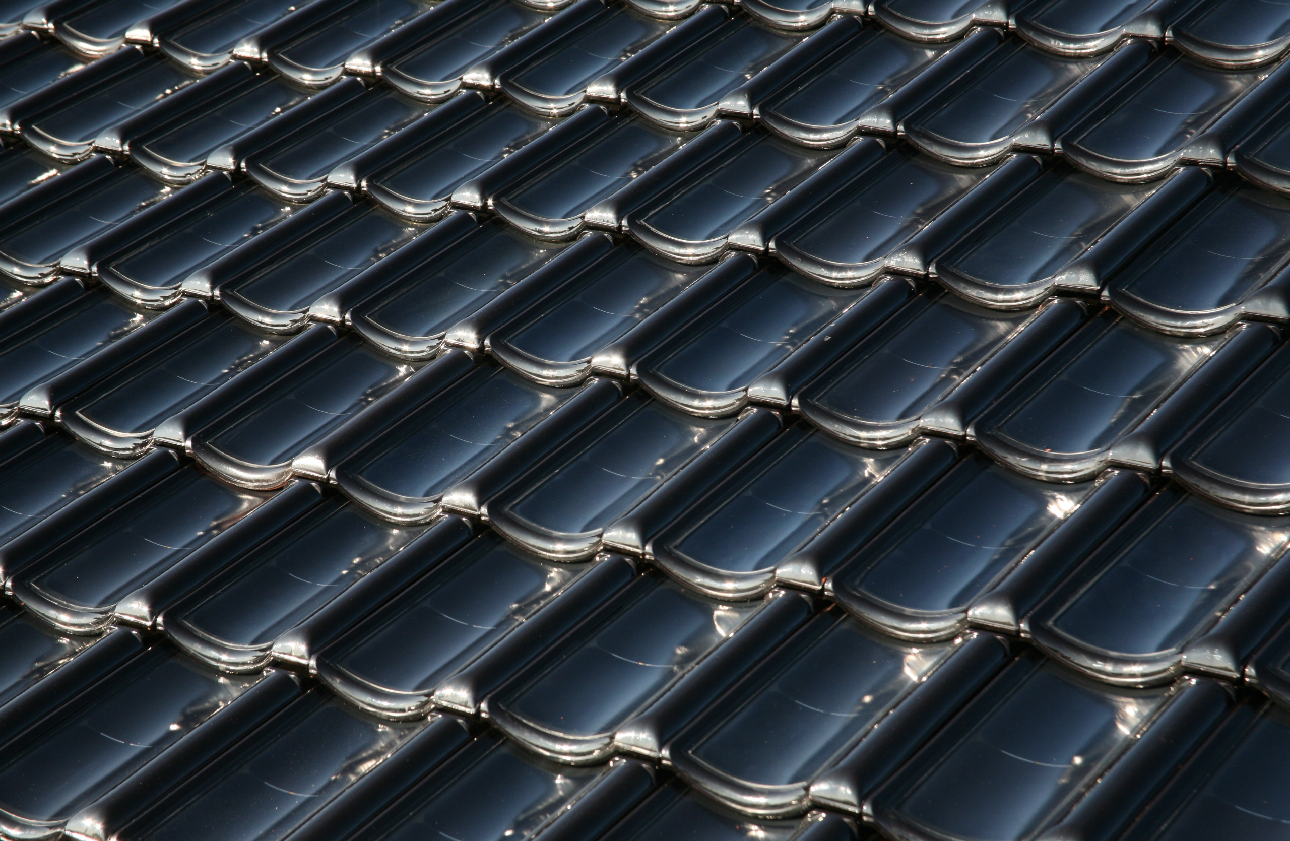 Close-up of dark solar rooftop tiles with glossy, overlapping modules reflecting sunlight.