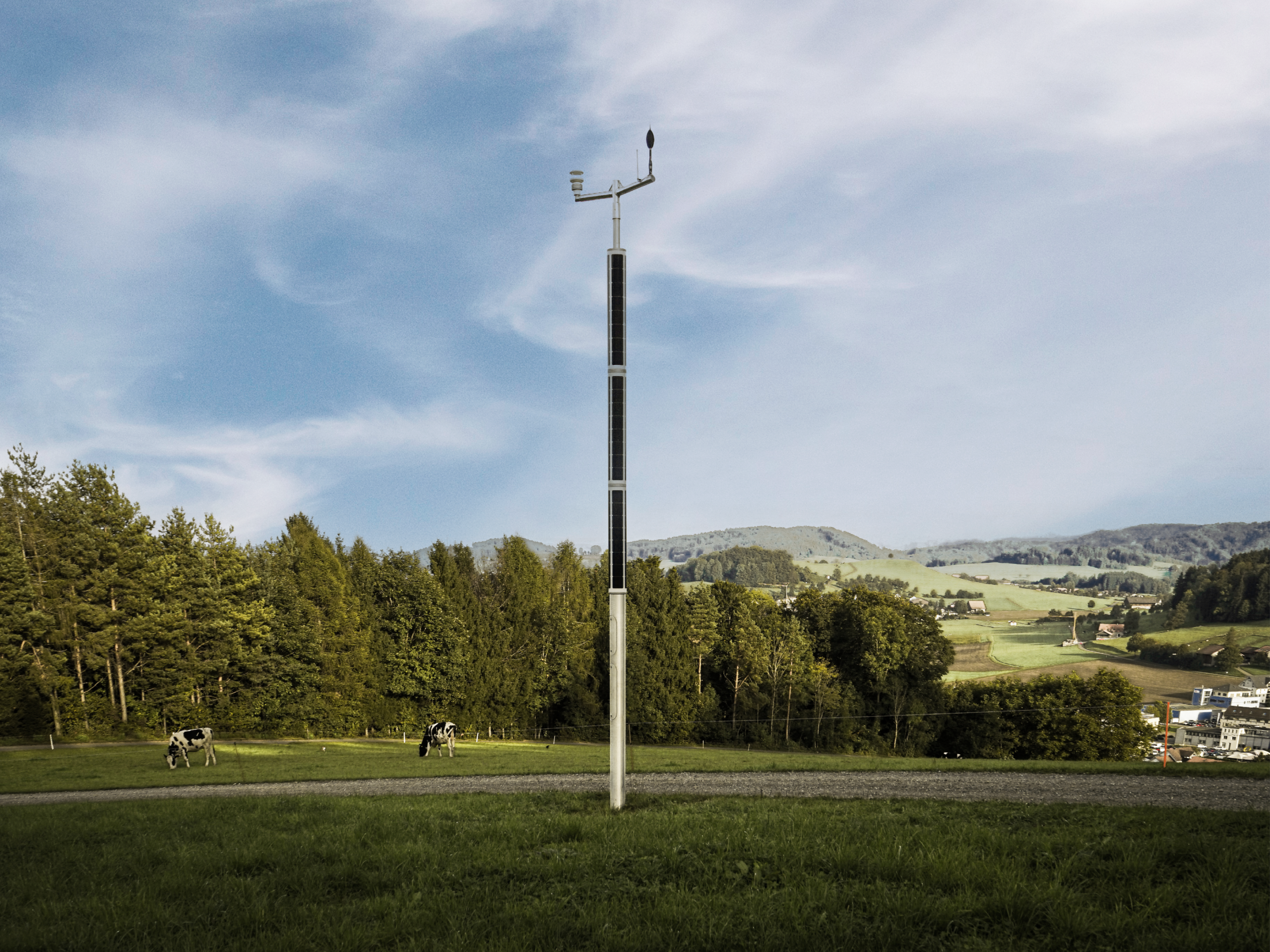 Solar pole with integrated sensors installed in a rural Swiss landscape with hills and grazing cows.